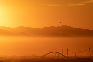 golden sunset, mountains above the fog in the background, and a helicopter in the air