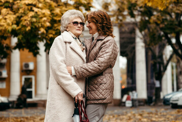 A young woman takes care of an elderly woman in a park against the backdrop of an autumn landscape