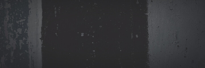 Dark wide panoramic background. Peeling paint on a concrete wall. Faded dark texture of old cracked flaking paint. Weathered rough painted surface with patterns of cracks. Shaded background for design