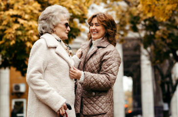 Fototapeta premium A young woman takes care of an elderly woman in a park against the backdrop of an autumn landscape