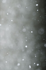 Bokeh of white snow on a square shape gray background. Falling snowflakes on night sky background,...