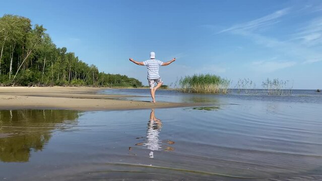 a young man does yoga on the beach in summer in sunny weather, does asana, Tree pose.