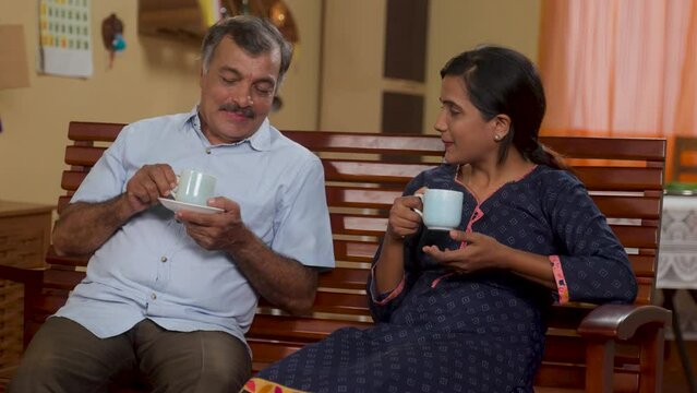 Joyful senior retired Indian father with talking with daughter while having tea at home - concept of family time, daily routine and sharing memories