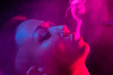 Close up portrait of asian woman with short hair smoking in neon light. 
