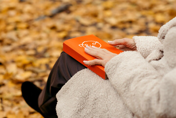 An older woman reading a book. She is sitting on the bench in the colorful park in the autumn