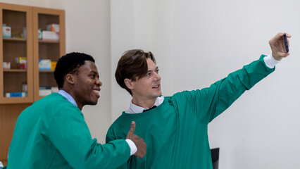 Two young doctors in uniform from different cultures having a conversation during a break in a surgery clinic. Friendship between young doctors. Doctors taking selfie.