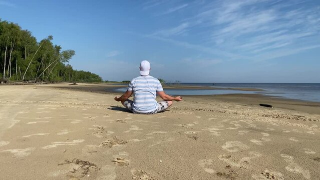 a young man does yoga on the beach in summer in sunny weather. does the lotus pose, meditation.
