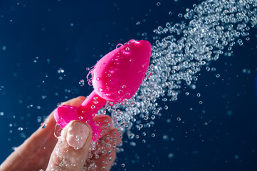 Woman washing pink anal plug under shower on blue background. 