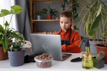 Teenage girl replanting flowers at home uses a laptop and watches an online training video on...