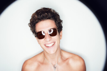 Man, sunglasses and smile in studio with spotlight, fashion or shirtless with edgy punk style by...