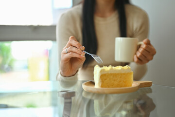 Cropped shot of young woman drinking coffee and eating diet cake at coffee shop during lunch break