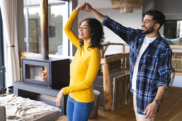 Happy biracial couple dancing and smiling in living room at home