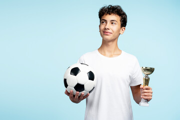 Portrait of attractive pensive teenage boy holding ball, win football competition. Sport concept
