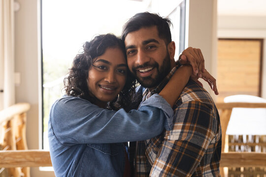 Happy biracial couple embracing and smiling in living room at home