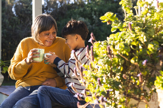 Happy biracial grandmother and grandson drinking tea sitting in garden