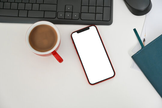 Flat lay, top view smartphone with blank screen, coffee cup and keyboard on white office desk