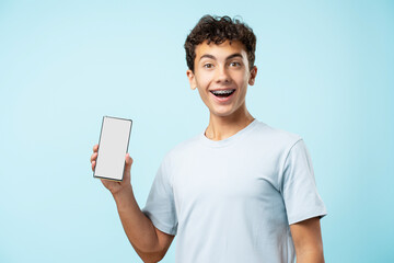 Portrait of happy teenage boy with braces holding mobile phone, showing screen isolated on blue background, mockup. Mobile app, technology concept  