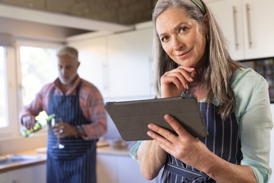 Portrait of happy senior caucasian couple cooking dinner, using tablet in kitchen