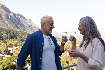 Happy senior caucasian couple drinking wine on balcony
