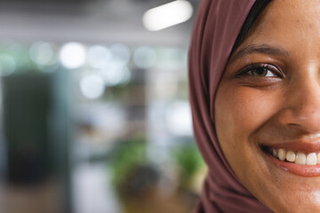 Portrait of happy biracial casual businesswoman with hijab in creative office, copy space
