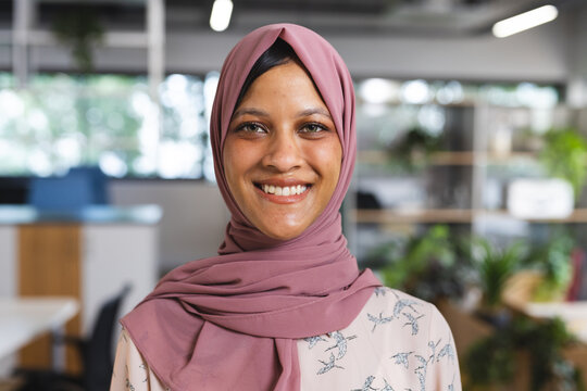 Portrait of happy biracial casual businesswoman with hijab in creative office - Powered by Adobe