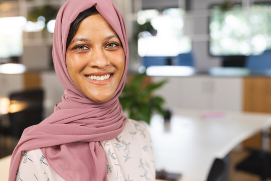 Portrait of happy biracial casual businesswoman with hijab in creative office, copy space