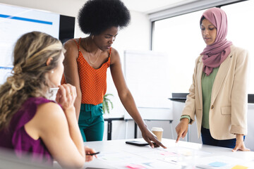 Busy diverse female colleagues at meeting discussing work with blueprint on table in office