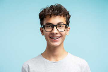 Portrait of smiling smart school boy with braces wearing glasses isolated on blue background....