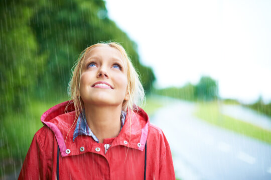 Woman, smile and raincoat in outdoor rainfall, wet and cold from weather, winter and nature. Happy female person, fashion and red jacket is cool, rain and looking up to sky by water, face and holiday