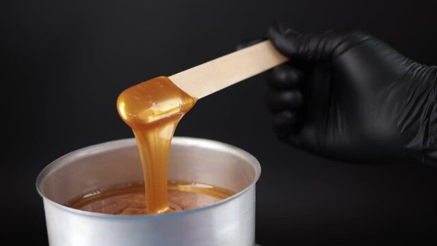 The depilatory wax is heated and melted in a special device. The master mixes the heating wax with a wooden spatula before the depilation procedure. Removing unwanted hair with wax.