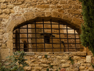passage avec barreaux en acier à travers un mur médiéval de pierre dorée et vue sur une tour à fenêtre derrière