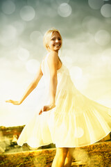 Fototapeta na wymiar Smile, bokeh and blonde woman in dress in the countryside, dance and freedom outdoor in summer. Happy, nature and person moving with energy on holiday, vacation or celebration for travel on field