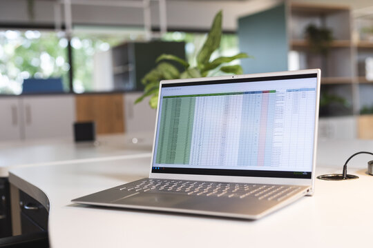 Empty creative office with wooden furniture, plants and laptop with data on table