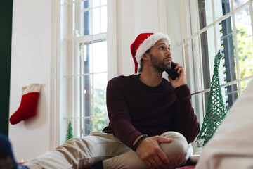 Though caucasian man in christmas hat talking on smartphone and looking out of window, copy space