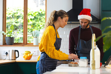 Happy caucasian couple in aprons and christmas hat baking in kitchen, copy space