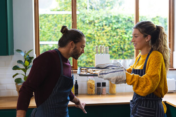 Happy caucasian couple holding freshly baked cookies and smelling them in kitchen