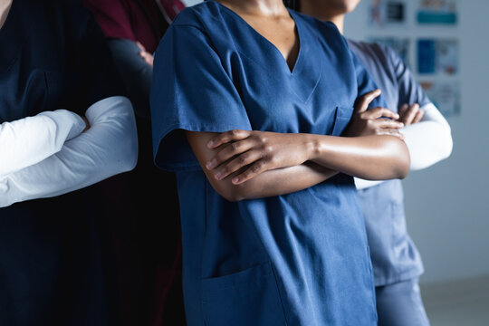 Midsection of diverse male and female doctors wearing scrubs crossing arms in corridor in hospital