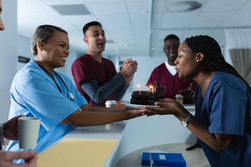 Happy diverse male and female doctors celebrating birthday at reception desk at hospital