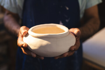Hands of senior biracial potter holding clay vase in pottery studio