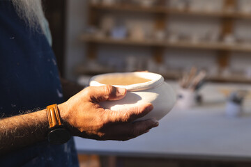 Hands of senior biracial potter holding clay vase in pottery studio
