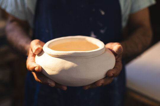 Hands of senior biracial potter holding clay vase in pottery studio
