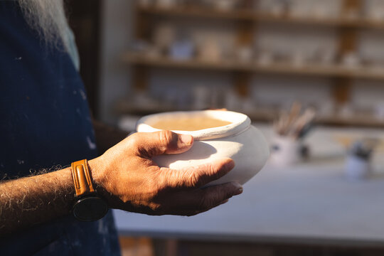 Hands of senior biracial potter holding clay vase in pottery studio - Powered by Adobe