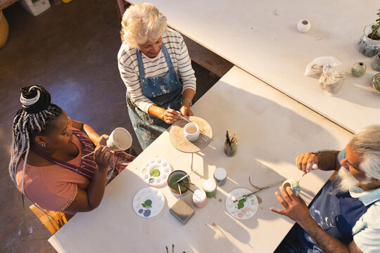Happy diverse group of potters glazing clay jugs in pottery studio