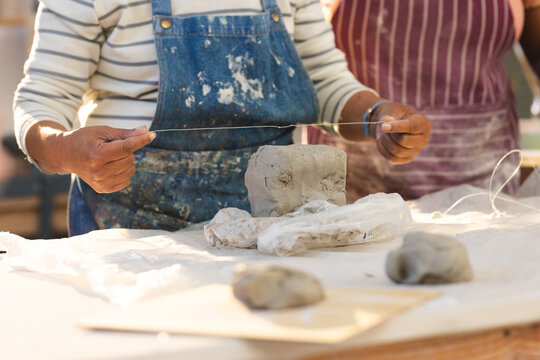 Mid section of biracial senior female potter cutting clay with wire in pottery studio - Powered by Adobe
