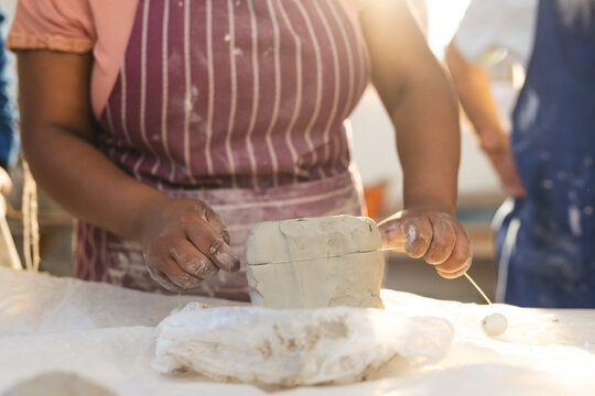 Mid section of african american female potter cutting clay with wire in pottery studio