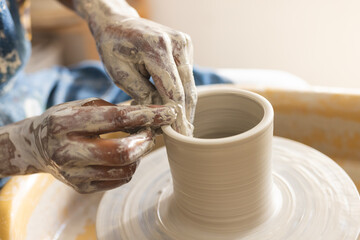 Hands of african american potter working on clay vase using potter's wheel in pottery studio