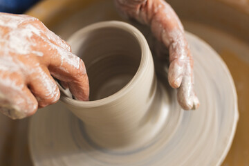 Hands of biracial senior potter with long beard using potter's wheel in pottery studio