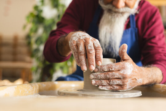 Focused biracial senior male potter working on clay vase using potter's wheel in pottery studio