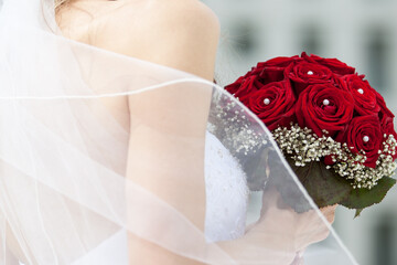 Braut in weissem Hochzeitskleid hält einen roten Rosenkranz in der Hand.