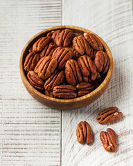 Peeled pecans in a wooden bowl on a white wooden background. Nuts.